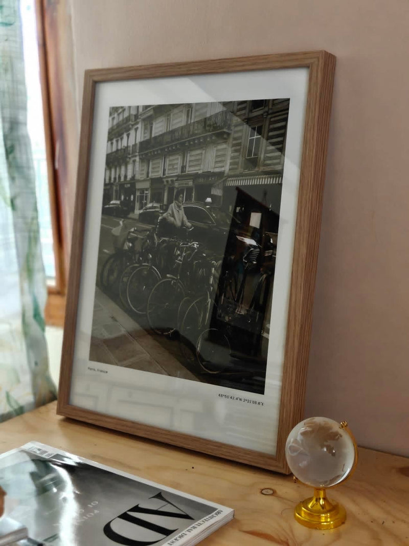 Karan's À Vélo print framed in warm oak on a desk